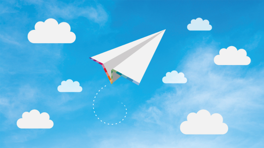 Paper plane with rainbow coloured stripes against a blue sky