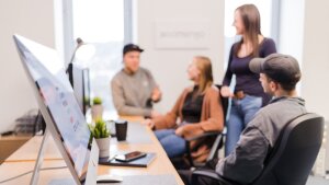 Blick ins Büro auf Schreibtisch, Bildschirm und Mitarbeitende