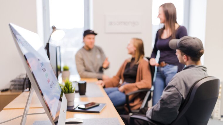 View into an office with a desk, a screen and employees