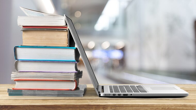 Bücherstapel und Laptop auf Holztischplatte